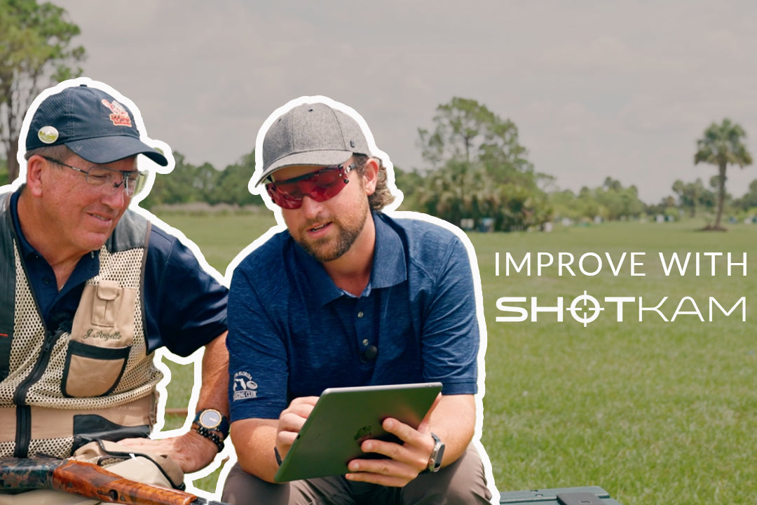ShotKam image featuring two men sitting outdoors, one holding a shotgun and the other reviewing something on a tablet. The text reads 'Improve with ShotKam,' with a grassy field and trees in the background.