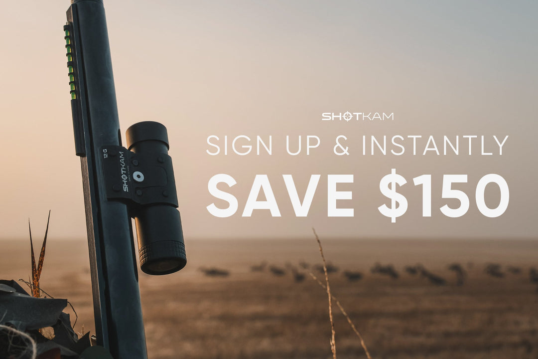 Hunter aiming shotgun with ShotKam camera mounted, ducks flying over water on a cloudy day.