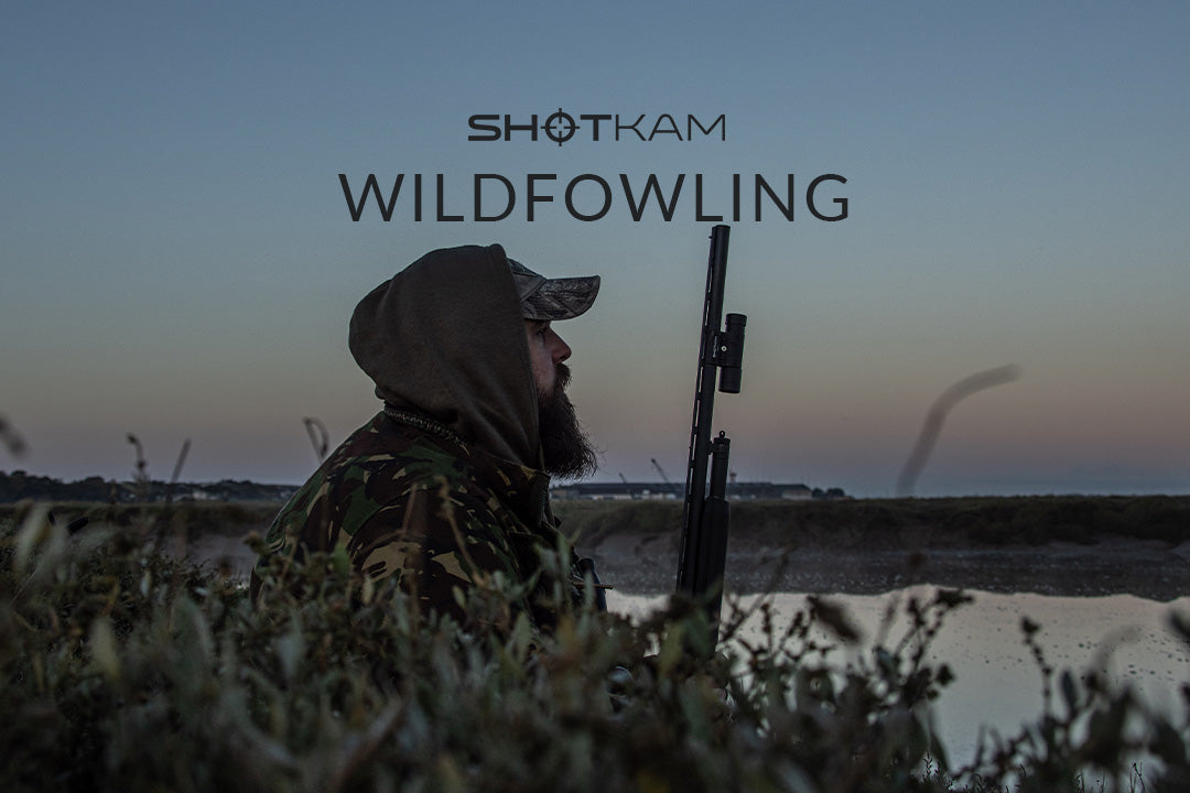 ShotKam blog cover photo featuring a hunter in camouflage gear sitting by a waterway at dusk, holding a shotgun. The text reads 'Wildfowling' with the ShotKam logo above, set against a serene landscape.
