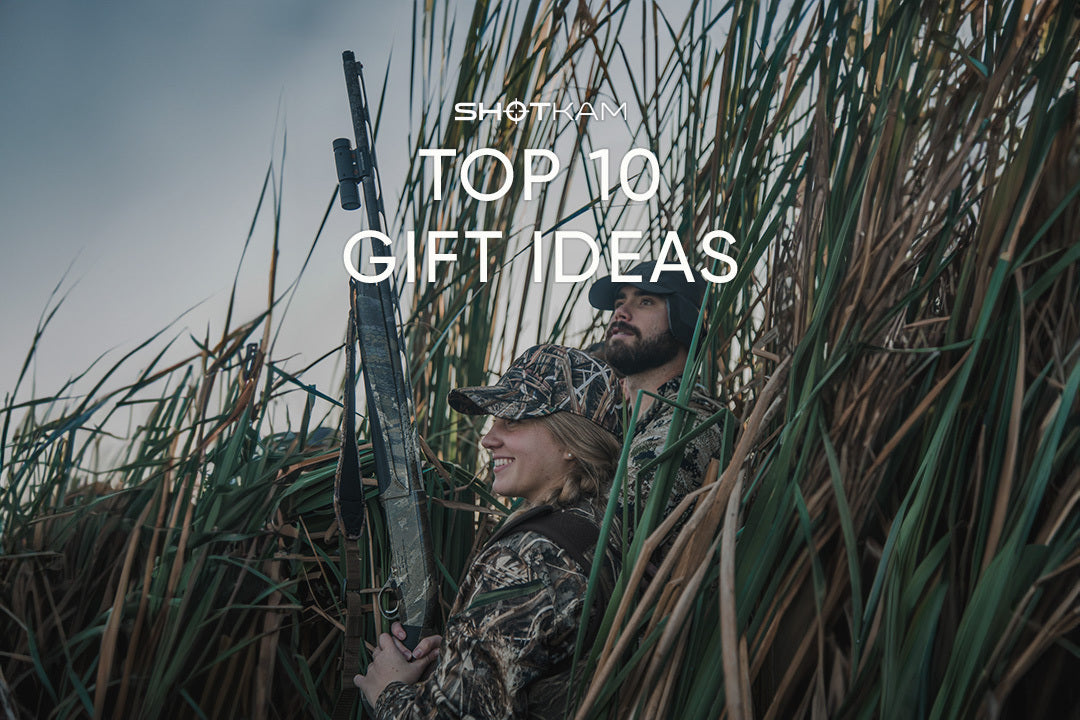 Two hunters in camouflage holding shotguns, standing in tall grass, with text overlay 'Top 10 Gift Ideas' by ShotKam USA.