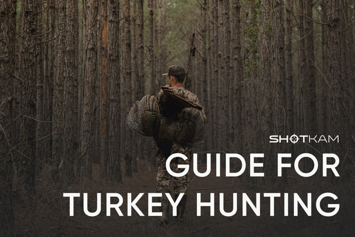 Hunter carrying a wild turkey through pine woods with ShotKam mounted on shotgun barrel
