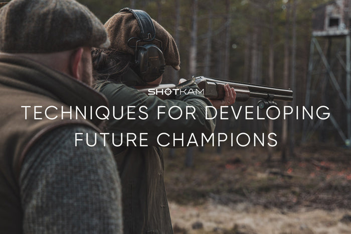 ShotKam thumbnail image featuring two people outdoors, one aiming a shotgun. The text reads 'Techniques for Developing Future Champions' against a wooded background.